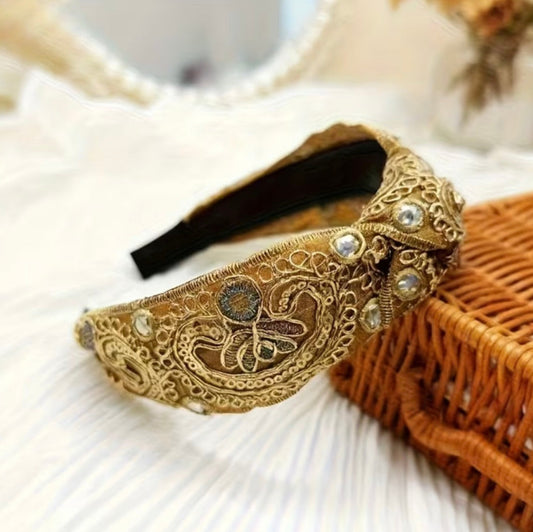 Decorative gold headband with intricate designs on a white surface.