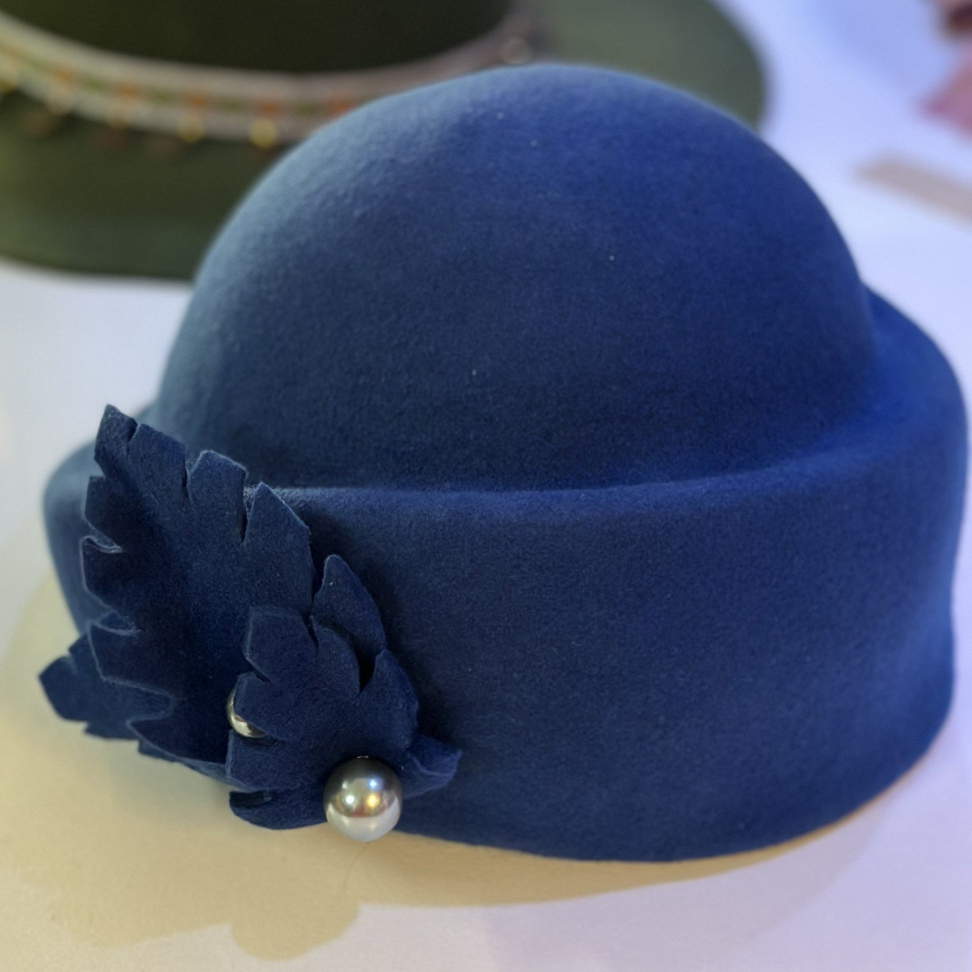 Blue felt hat with a decorative flower and pearl on a white surface